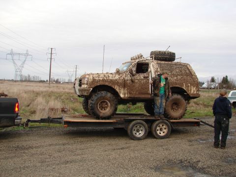 1996 Ford Bronco - A heavily mud-caked SUV is being transported on a trailer, with two people observing.