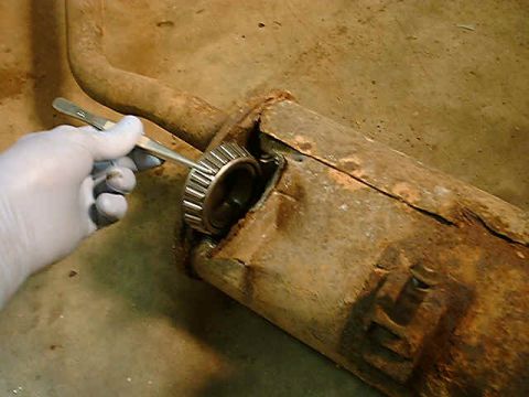 1989 Ford Bronco - A gloved hand uses a tool to remove a bearing from a heavily rusted exhaust pipe section.