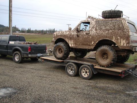 1996 Ford Bronco - A heavily mud-caked SUV is transported on a trailer behind a pickup truck.