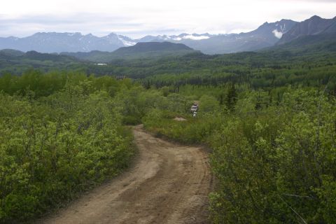 2003 Jeep TJ - Two SUVs navigate a dirt road through a lush green landscape with snow-capped mountains in the distance.
