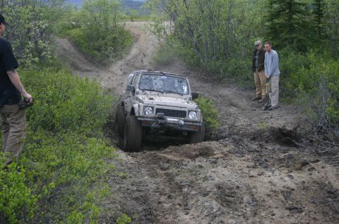 2003 Jeep TJ - A Suzuki Samurai navigates a challenging muddy off-road course, with onlookers observing the action.