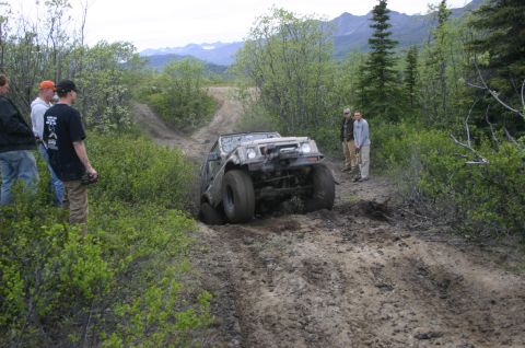 2003 Jeep TJ - An off-road vehicle navigates a muddy trail, with onlookers observing the challenging terrain.
