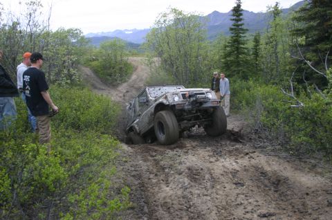 2003 Jeep TJ - An off-road vehicle navigates a challenging muddy terrain with onlookers observing the difficult maneuver.
