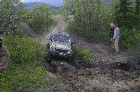 2003 Jeep TJ - Suzuki Samurai tackling a challenging muddy incline during an off-road event.