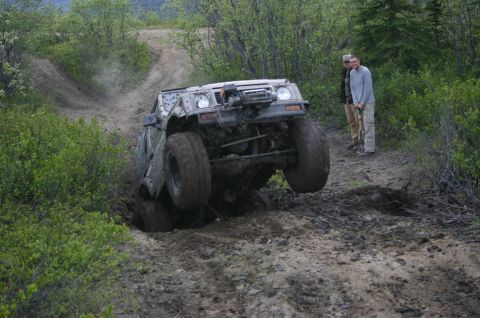 2003 Jeep TJ - An off-road vehicle navigates a challenging muddy obstacle on a wooded trail.
