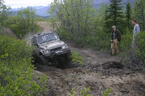 2003 Jeep TJ - Suzuki Samurai navigating a challenging muddy track with onlookers present.