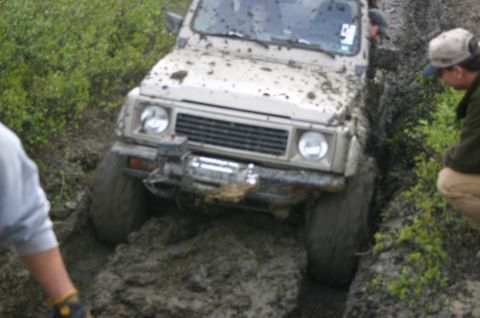2003 Jeep TJ - A beige off-road vehicle navigates a muddy trail, with people observing the difficult terrain.