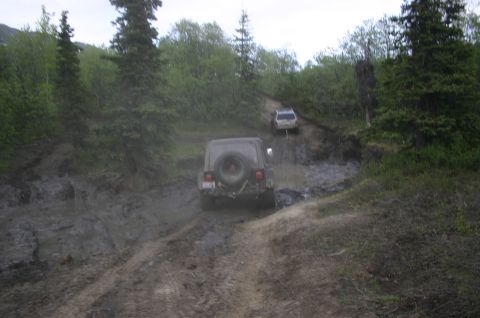 2003 Jeep TJ - A 2003 Jeep TJ tackles a challenging muddy off-road path, followed by another vehicle.