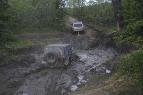 2003 Jeep TJ - Two off-road vehicles navigate a challenging muddy trail, one appears stuck.