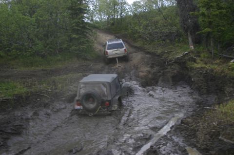 2003 Jeep TJ - Two off-road vehicles navigate a challenging muddy track through a forest.