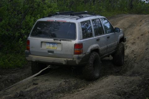 2003 Jeep TJ - A lifted silver Jeep Grand Cherokee navigates a muddy off-road trail.