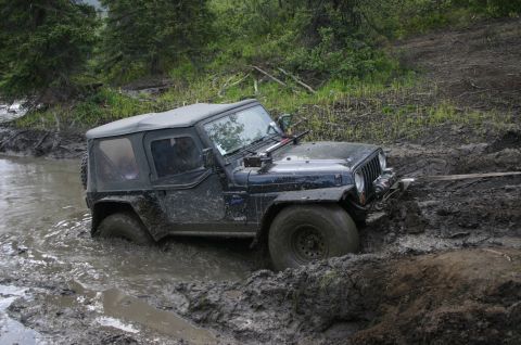 2003 Jeep TJ - A black 2003 Jeep TJ is stuck in thick mud, with its tires submerged.