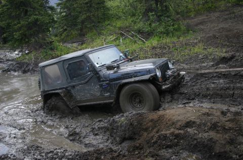 2003 Jeep TJ - A Jeep Wrangler is stuck in a muddy trail, with trees and foliage in the background.
