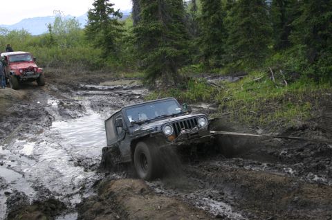 2003 Jeep TJ - A black 2003 Jeep TJ navigates a challenging muddy trail, while a red Jeep waits behind.