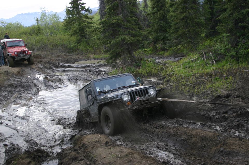 Black 2003 Jeep TJ struggling through deep mud with a tow strap attached