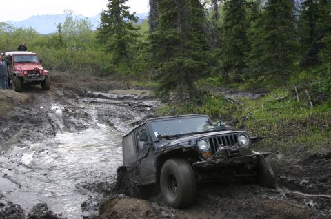 2003 Jeep TJ - Two Jeeps tackle a challenging muddy off-road course in a wooded area.