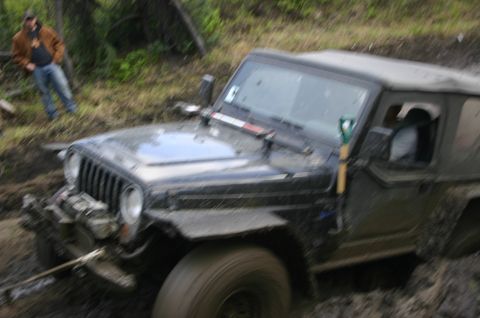 2003 Jeep TJ - A Jeep Wrangler is stuck in thick mud, with a person observing from the side of the trail.
