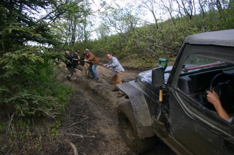 2003 Jeep TJ - A group of people pull a stuck Jeep Wrangler TJ out of the mud with a rope during an off-road event.
