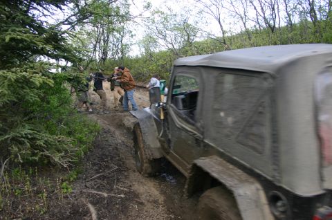 2003 Jeep TJ - People help pull a muddy Jeep TJ out of a ditch during an off-road event.