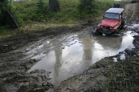 2003 Jeep TJ - A red Jeep Wrangler navigates a challenging muddy trail during an off-road event.