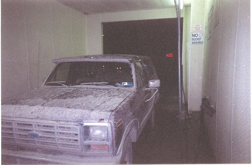 Mud-covered Ford Bronco in a car wash bay next to a No Bucket Washing sign