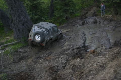 2003 Jeep TJ - An off-road vehicle navigates a challenging muddy terrain, with a person observing from higher ground.