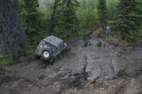 2003 Jeep TJ - A 2003 Jeep TJ navigates a challenging muddy off-road course in a forest.