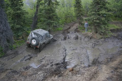 2003 Jeep TJ - A 2003 Jeep TJ struggles through a challenging mud obstacle during an off-road event in a wooded area.