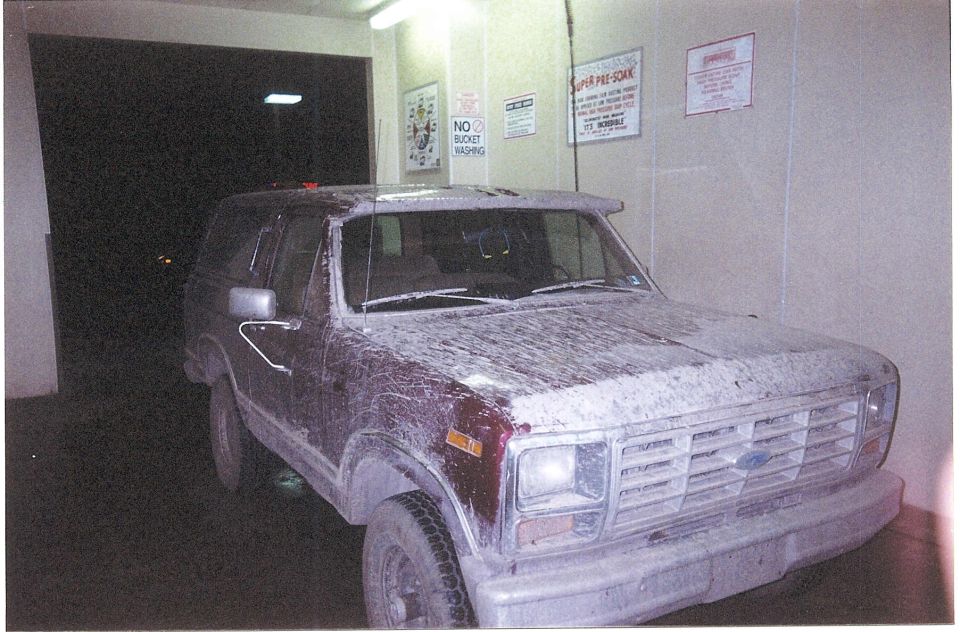 Mud-covered dark red Ford Bronco in a car wash bay with a No Bucket Washing sign on the wall