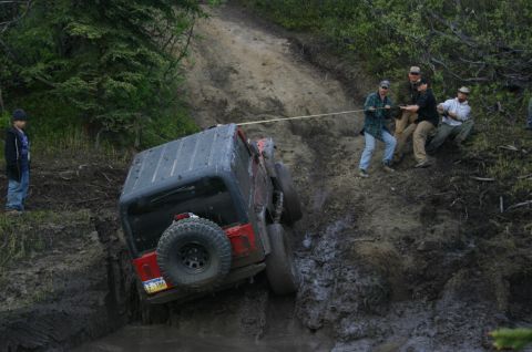 2003 Jeep TJ - A Jeep TJ is stuck in the mud and being pulled by a group of people.