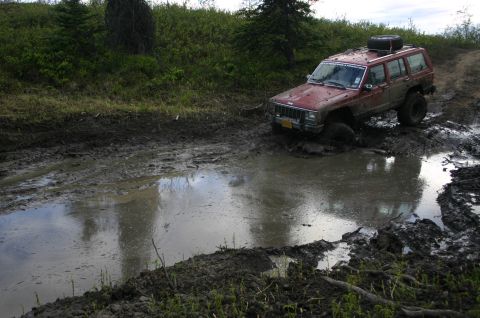 2003 Jeep TJ - Off-roading adventure: a red Jeep Cherokee XJ navigates a challenging muddy terrain.