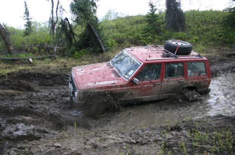 2003 Jeep TJ - A red Jeep Cherokee XJ is stuck in deep mud during an off-road event.
