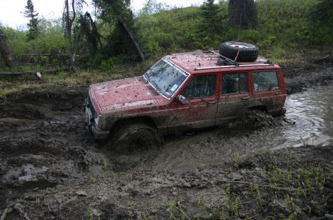2003 Jeep TJ - This red Jeep Cherokee is deeply stuck in thick mud on an off-road trail.