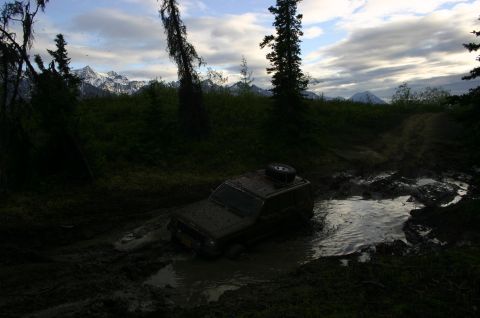 2003 Jeep TJ - A Jeep Wrangler TJ navigates a muddy trail with mountains in the background.