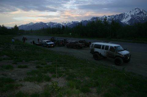 2003 Jeep TJ - Several vehicles are gathered on a dirt road near a mountain range at dusk.