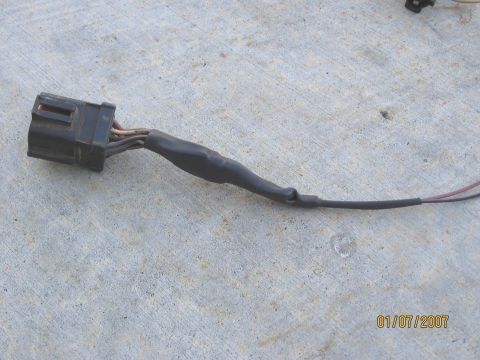 1994 Ford Bronco - A close-up view of a wiring harness connector with wires extending from it, taped for protection.