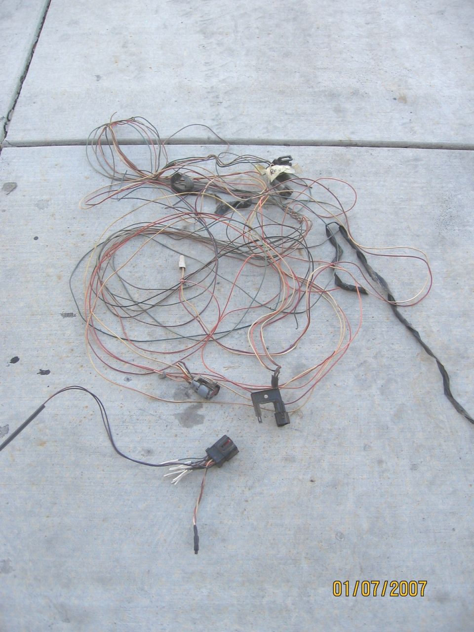 Tangled vehicle wiring harness with multiple connectors lying on concrete