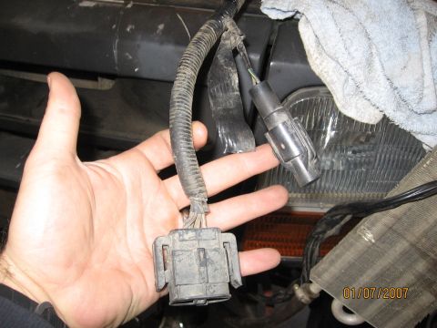 1994 Ford Bronco - A hand holds a wiring harness connector in front of a 1994 Ford Bronco's headlight and grille assembly.