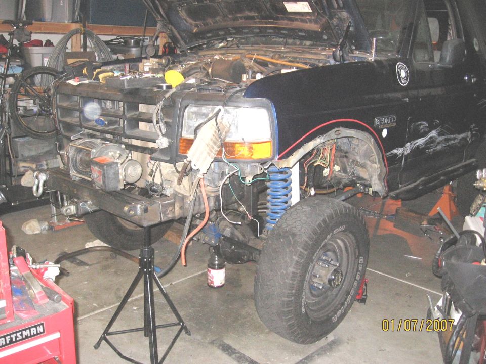 Dark blue Ford Bronco torn down in a garage, fender off and front end on a jack stand