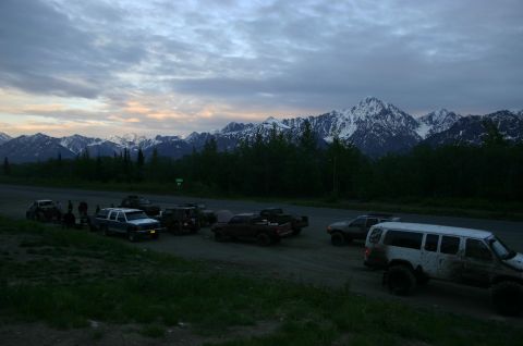 2003 Jeep TJ - A group of off-road vehicles gather on a dirt road with a dramatic mountain backdrop under a cloudy sky.