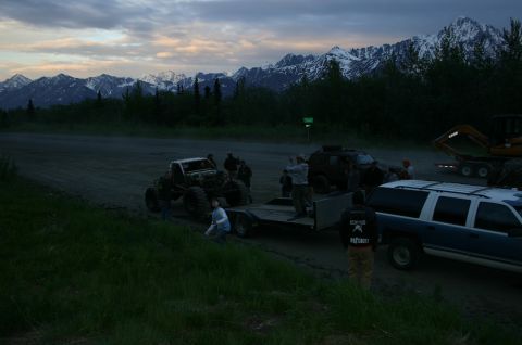 2003 Jeep TJ - Several vehicles gathered near a mountain range, including an off-road vehicle being loaded onto a trailer.
