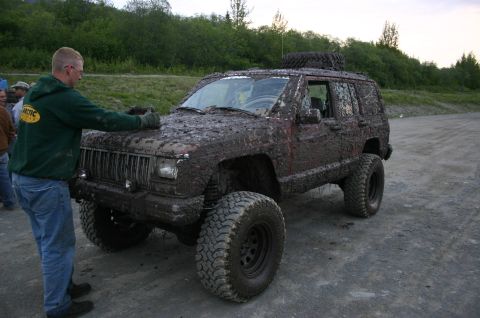 2003 Jeep TJ - A man wipes mud off a heavily soiled Jeep Cherokee XJ after an off-road event.