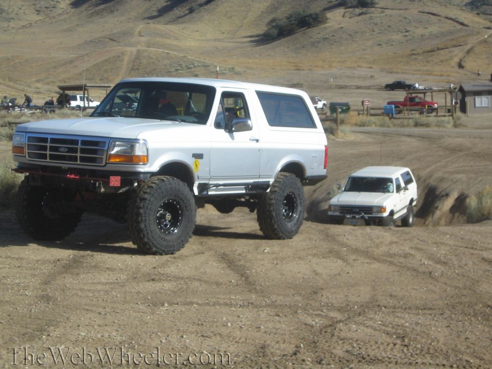 Lifted white Ford Bronco and another white SUV driving on a dirt trail