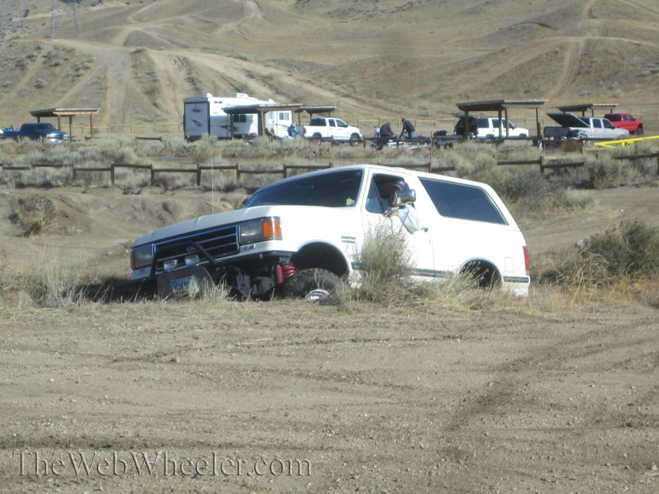 white SUV with aftermarket bumper stuck in dirt, other vehicles and campers in background