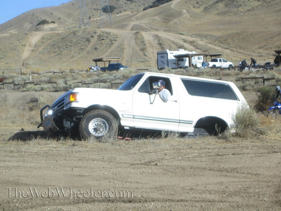 White SUV stuck in dirt, front bumper damaged, driver visible