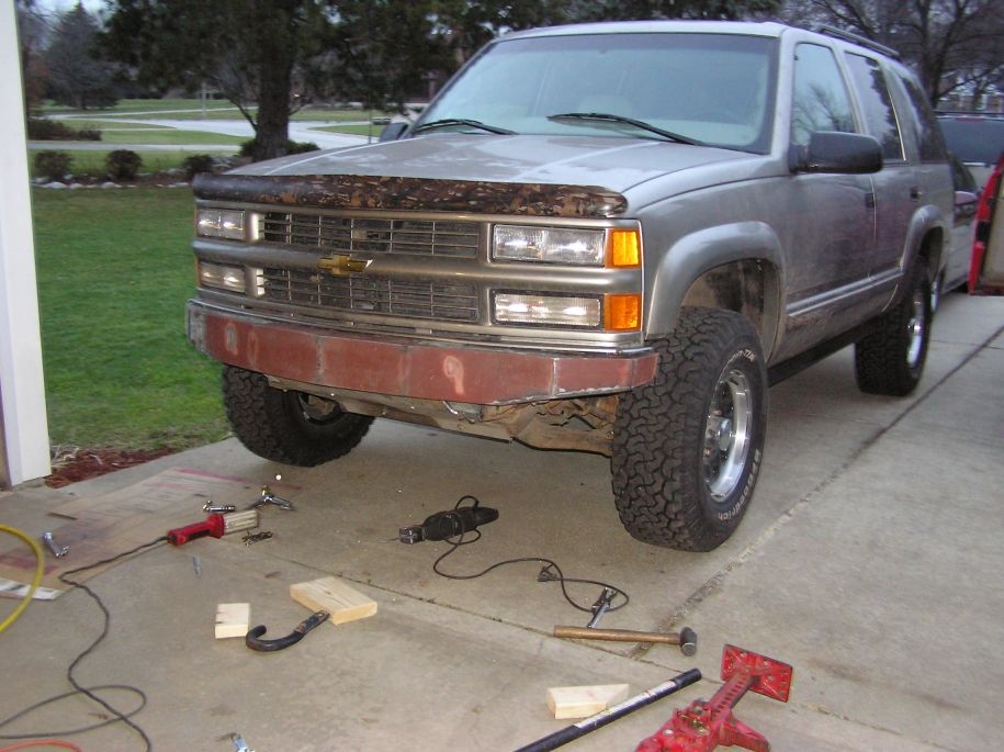 Silver Chevrolet Tahoe with a red primer front bumper and a camouflage bug deflector