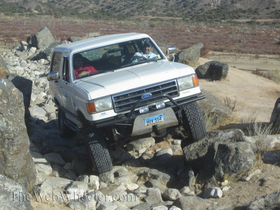 White Ford Bronco navigating rocky terrain, front bumper with license plate HOV 554