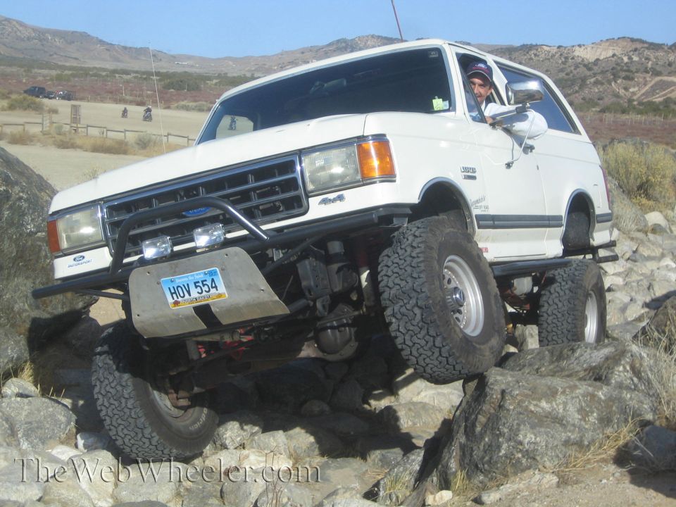 White off-road SUV with lifted suspension and large tires climbing over rocks