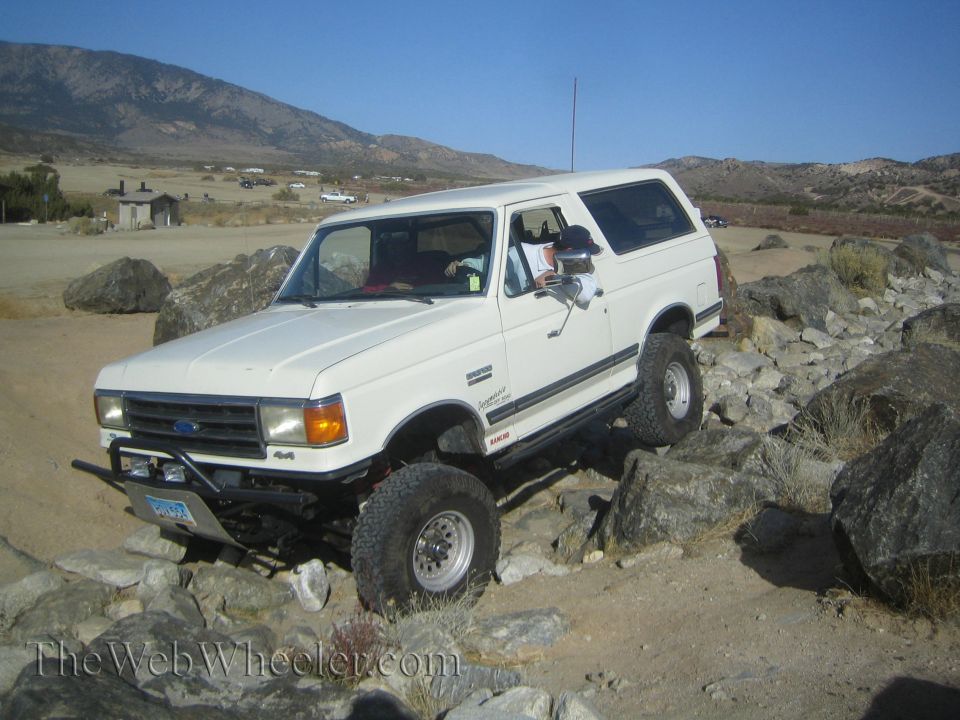 White 1987 Ford Bronco off-roading on rocks. "4x4" badge visible