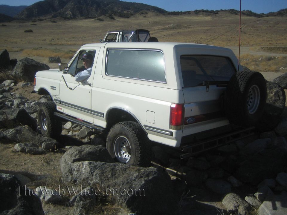 White Ford Bronco navigating rocky terrain. Another SUV is visible in the background